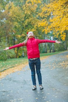 Cute girl walking in the autumn park. Rain, yellow leaves, tree. Vertical view