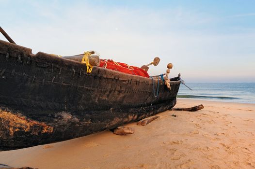 Old boat with fishing net on sandy shore. In Goa