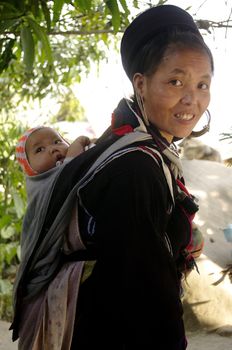 A Black Dao woman and her baby. All women carry their baby in the back. They are well all day, despite the hard work the fields, rocked back on their mother