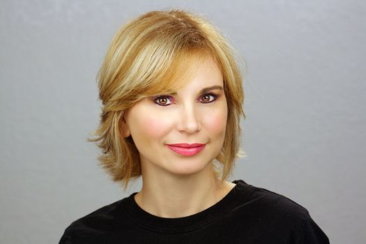 Close-up of a lovely young woman with sandy-blonde hair, plain grey background.