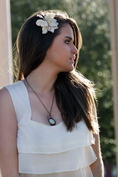 Close-up of a lovely young woman outdoors, backlit by the sun.  Her torso faces the camera, but her head is turned profile to her left.