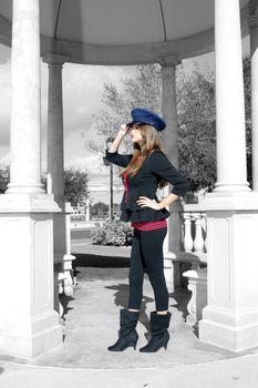 Full-length shot of a beautiful young brunette wearing a stylized costume that's remeniscent of the old British Guard.  The model and her wardrobe are in color; everything else is black-and-white.