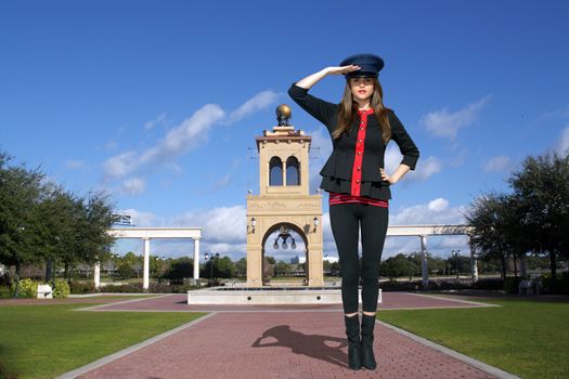 Full-length shot of a beautiful young brunette wearing a stylized costume that's remeniscent of the old British Guard, outdoors on a bright, sunny day.