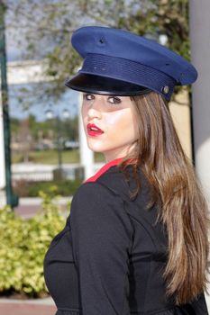 Close-up shot of a beautiful young brunette wearing a stylized costume that's remeniscent of the old British Guard, outdoors on a bright, sunny day.