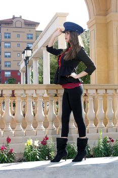 Full-length shot of a beautiful young brunette wearing a stylized costume that's remeniscent of the old British Guard, outdoors on a bright, sunny day.