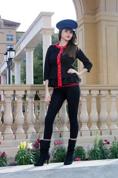 Full-length shot of a beautiful young brunette wearing a stylized costume that's remeniscent of the old British Guard, outdoors on a bright, sunny day.