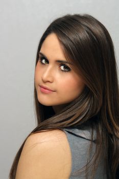 A studio close-up of a lovely young brunette with long, luscious hair and a neutral facial expression, looking back at the camera over her left shoulder.