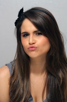 A studio close-up of a lovely young brunette with long, luscious hair and pursed or puckered lips.