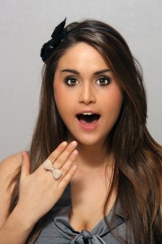 A studio close-up of a lovely young brunette with long, luscious hair and a surprised or shocked facial expression.