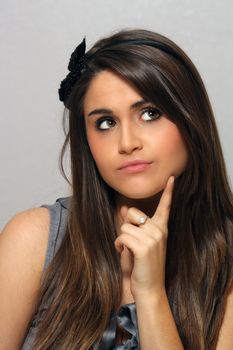 A studio close-up of a lovely young brunette with long, luscious hair and a wondering, curious, or perhaps undecided facial expression.