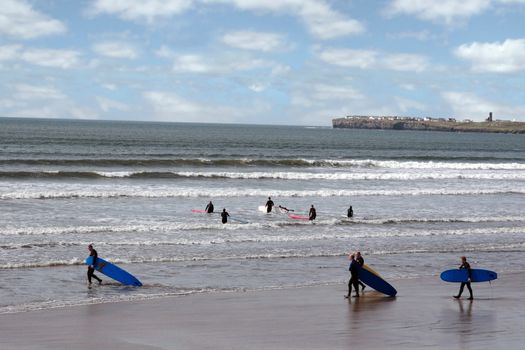 surfers walking on the beach in lahinch county clare ireland on a beautiful day