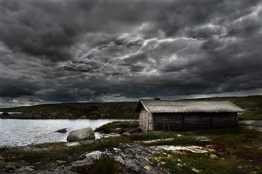 A lightning strikes over an old shed by a lake in the norwegian mountains