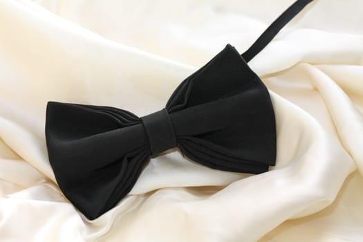 A black silk bow-tie on white satin, grooms accessory on his wedding day