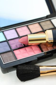 A palet with different shades of eye shadow, pink lipstick and a brush