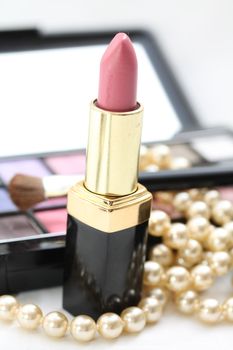 A pink lipstick with a pearl necklace, eye shadow palet in the back