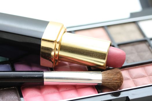 A palet with different shades of eye shadow, pink lipstick and a brush