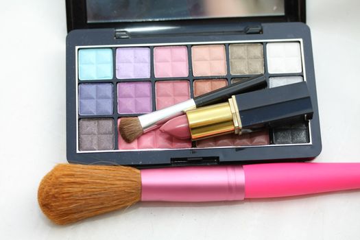 A palet with different shades of eye shadow, pink lipstick and a brush