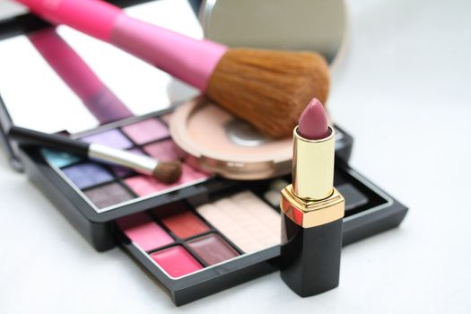 A pink lipstick, eye shadow palet and other cosmetics in the back