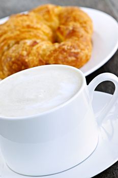 Latte coffee with frothed milk and fresh croissant