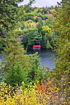 Boathouse on lake through fall forest with colorful trees