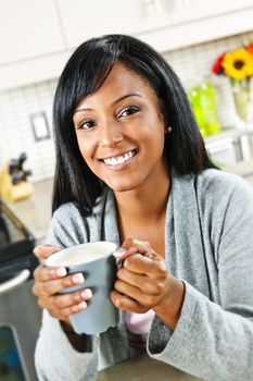 Smiling black woman holding coffee cup in modern kitchen interior