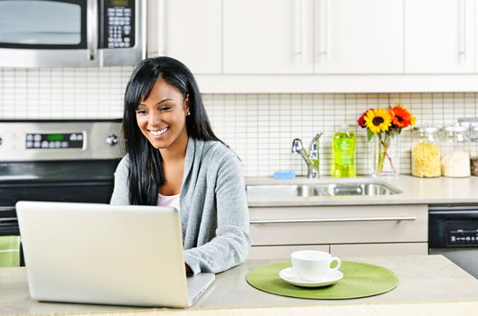 Smiling black woman using computer in modern kitchen interior