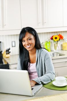 Smiling black woman using computer in modern kitchen interior