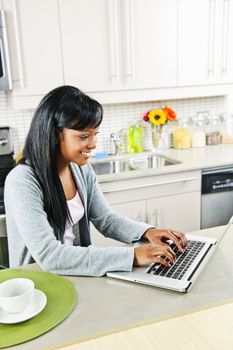 Smiling black woman using computer in modern kitchen interior