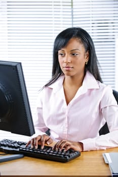 Portrait of serious young black business woman at desk typing on computer