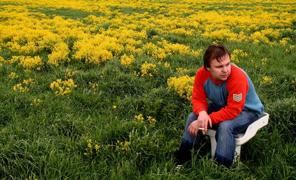 In the field on a toilet bowl. In a blossoming yellow field the young man sits on a toilet bowl.