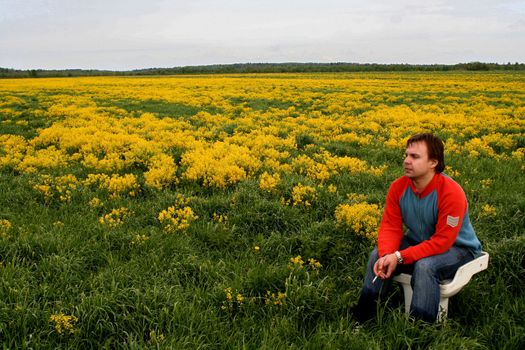 In the field on a toilet bowl. In a blossoming yellow field the young man sits on a toilet bowl.