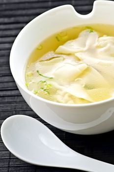 Wonton soup in white bowl with spoon