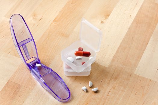 Pill cutter with pillboxes and cutted pills on wooden table