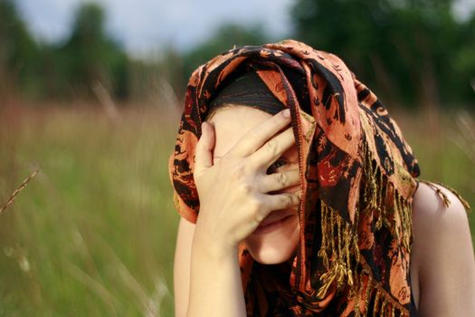 Natural beautiful girl with traditional kerchief over head looking through fingers and flirting. Outdoor shot.