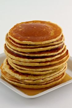 Stack of homemade pancakes with syrup on a white plate.