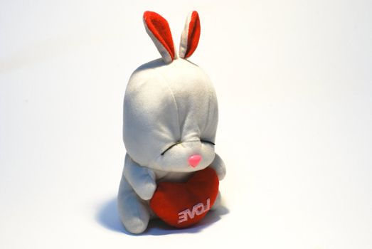 Rabbit sits and holds in paws red heart, a symbol of love 

