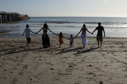 A family of 6 walk hand-in-hand toward the ocean.