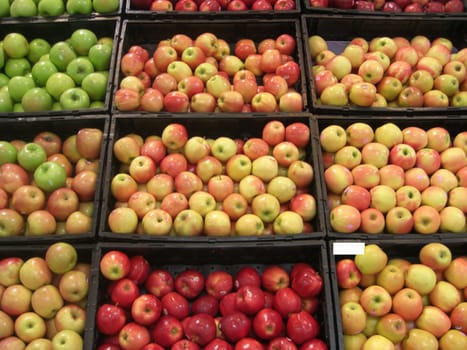 A stack of fresh, juicy and deliciously looking apples in a variety of colors are neatly displayed inside bins at a farmers market.
