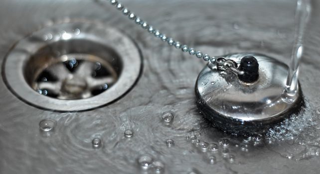 Macro shot of a plug in a sink with running water and water bubbles