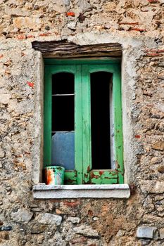 Decayed window with paint bucket on window-sill, broken glass and stone wall