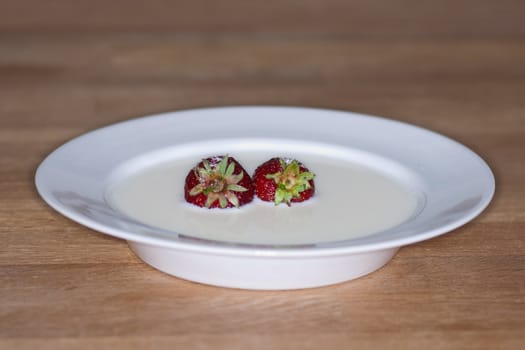 White saucer with fresh strawberries in milk with sugar poured over. Placed on wooden table