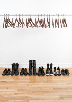 Row of black shoes and boots on a wooden floor, and empty hangers on a rod.