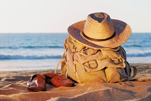 Knapsack, wicker hat and sandal on the sandy beach