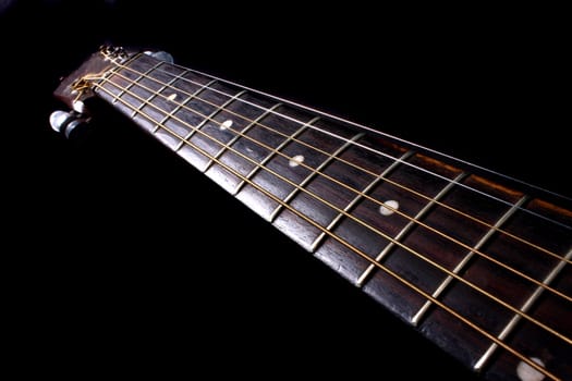 The fretboard of an acoustic guitar, on black background.