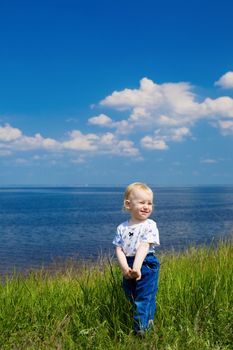 small girl in green grass over the blue sky near the river