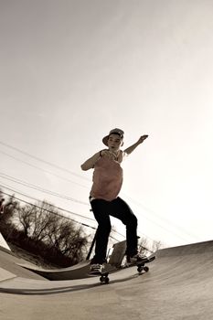 A young man skateboarding down a ramp at the skate park in sepia tone.