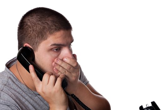 A young man on the phone places his hand on his mouth in disbelief of the news he has just heard.