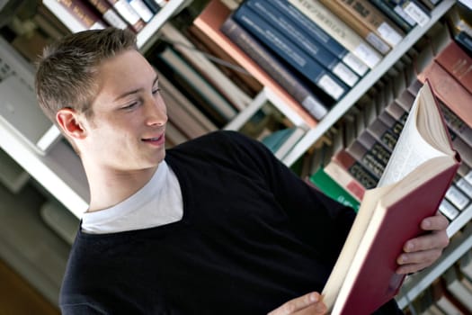 A young college aged man reading a book at the library.