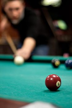 A young man lines up his shot as he breaks the balls for the start of a game of billiards. Shallow depth of field.