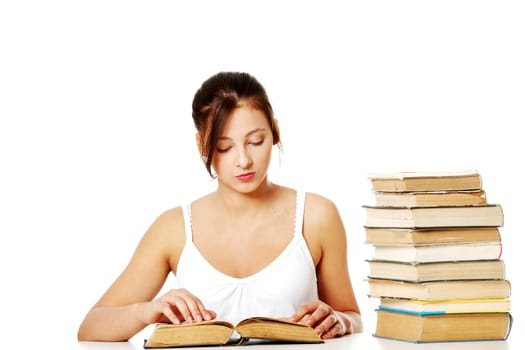 Young pretty caucasain girl sitting and reading a book near pile of books.